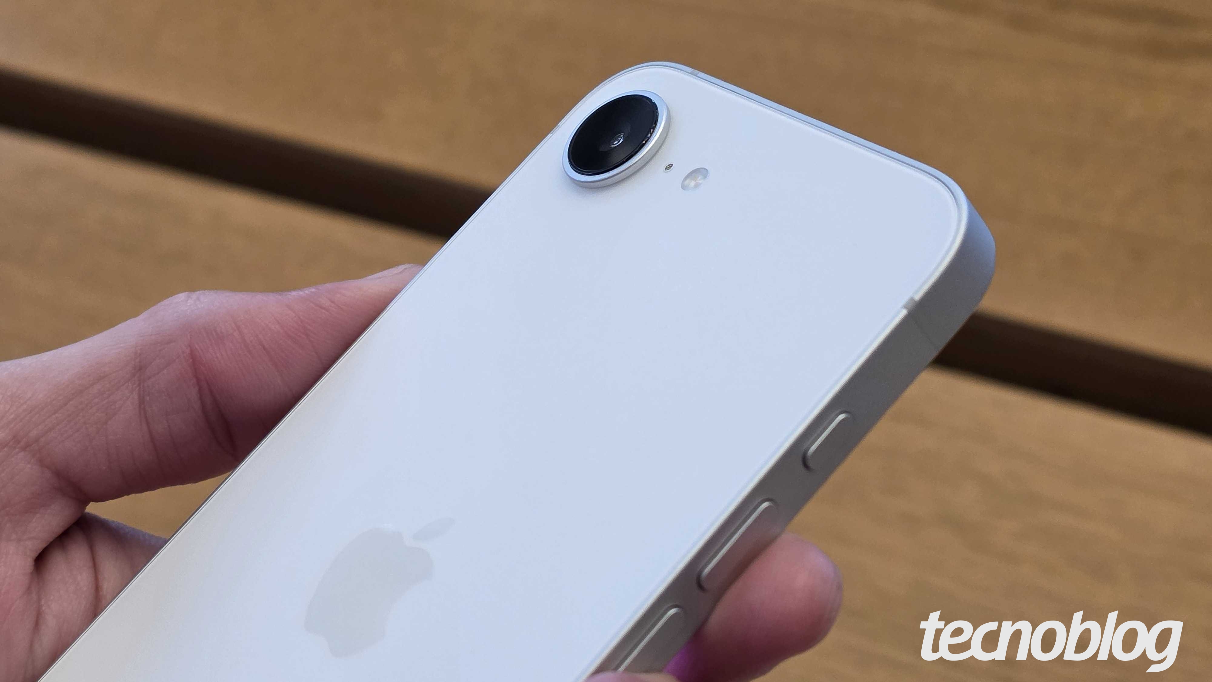 Imagem mostra um iPhone 16e sendo segurado em uma mão. A parte traseira está para cima.