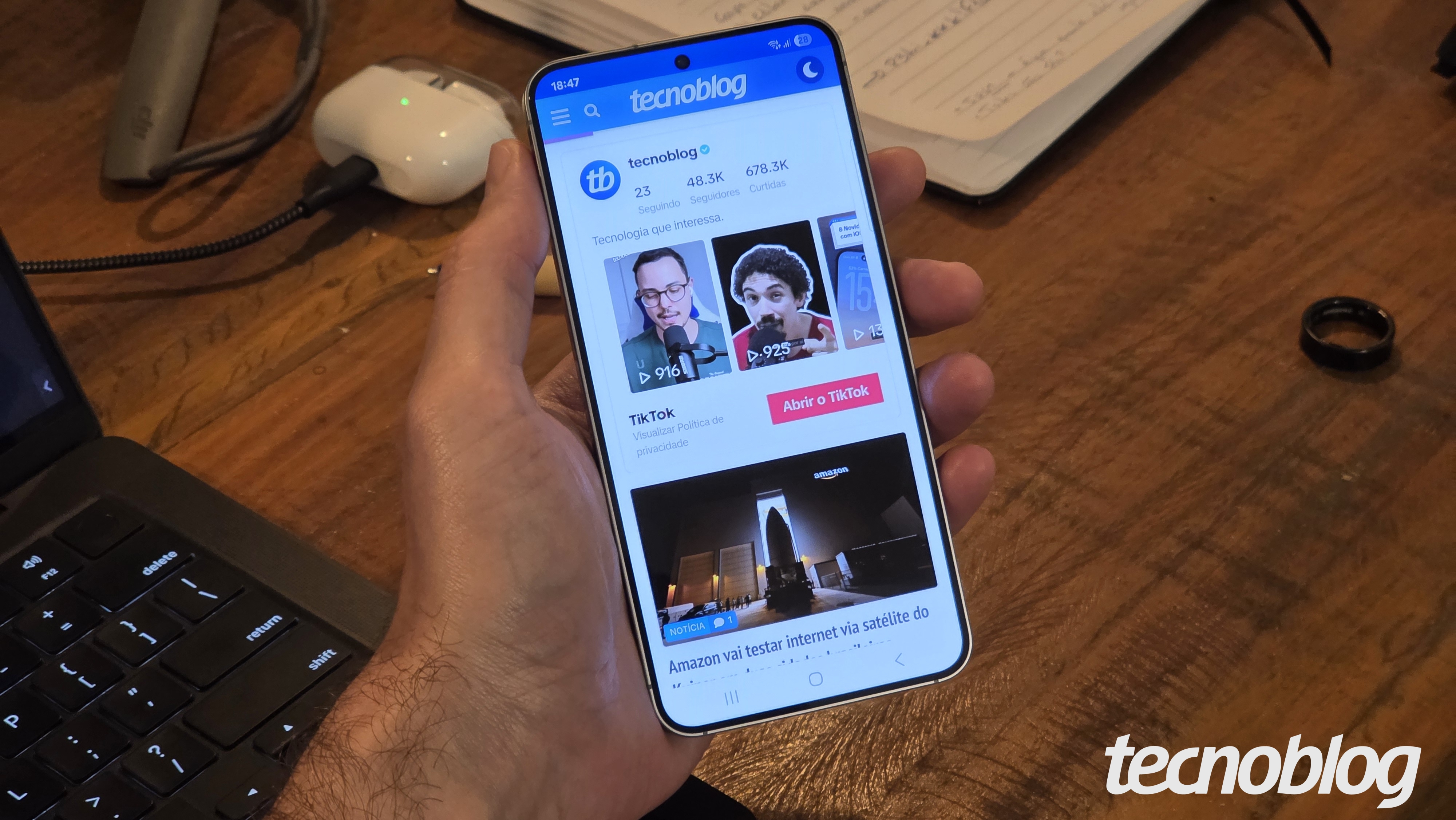 Mão segurando Galaxy S25 com tela ligada mostrando perfil do Tecnoblog no TikTok